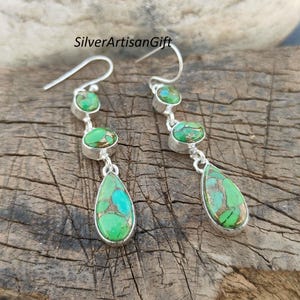 Op de afbeelding: Een paar zilveren oorhangers met groene turquoise stenen. De oorbellen hebben een traanvormige steen aan de onderkant en twee ronde stenen erboven.