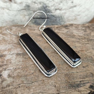 May include: A pair of silver earrings with black rectangular stones. The stones are set in a silver frame with a double border. The earrings have a hook closure.