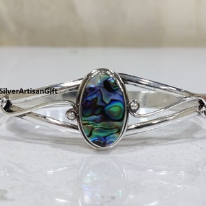 Puede incluir: Pulsera de plata con una incrustación ovalada de concha de abulón verde, azul y morado.
