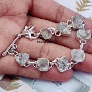 May include: A silver bracelet with a toggle clasp features clear, faceted, rough-cut gemstones.  The bracelet is made of sterling silver and has a polished finish.