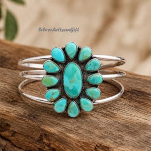 May include: A silver cuff bracelet featuring a central oval turquoise stone surrounded by twelve smaller teardrop-shaped turquoise stones. The metal band consists of three parallel silver wires. The text SilverArtisanGift is visible above.