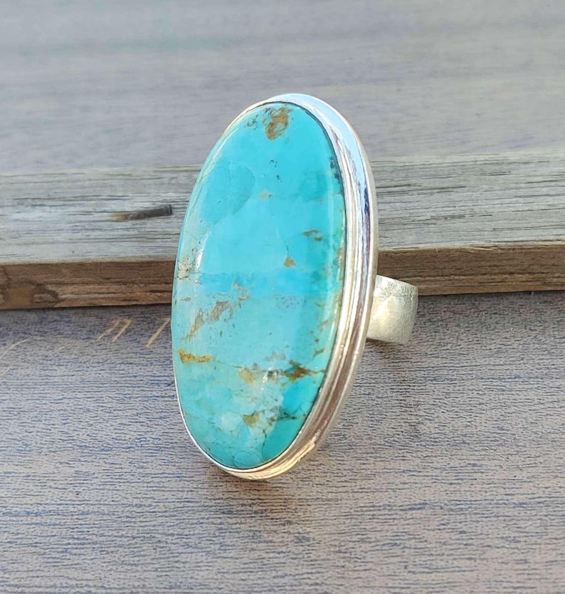 May include: A turquoise oval ring set in sterling silver. The turquoise is a vibrant blue-green color with brown veins and a smooth, polished finish.