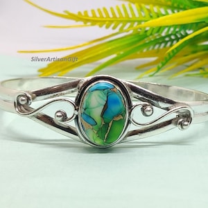 May include: A silver-toned bracelet with an oval-shaped, multi-colored stone. The stone features shades of green, blue, and brown. The bracelet has a decorative, swirling design on either side of the stone.