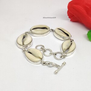 May include: A silver bracelet with a chain and a clasp. The bracelet is adorned with five white cowrie shells.
