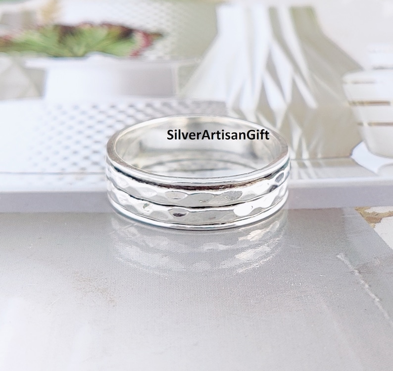 May include: A silver spinning ring with a hammered texture. The ring is made of sterling silver and has a simple, elegant design.