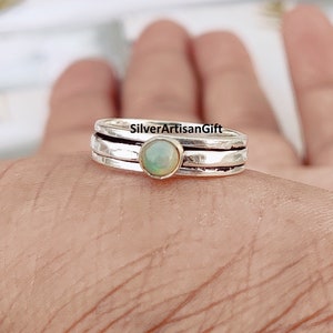 Può includere: Un anello d'argento con tre bande e una piccola pietra di opale rotonda di colore verde chiaro al centro.
