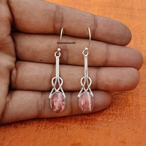 May include: A pair of silver dangle earrings with pink and white oval-shaped stones. The earrings have a delicate knot design.