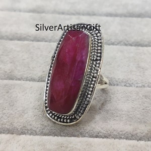Op de afbeelding: Een zilveren ring met een grote, ovale, rode edelsteen die is gezet in een getextureerde zilveren bezel. De ring heeft een eenvoudige band.