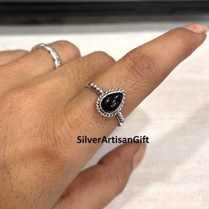May include: A silver ring featuring a black teardrop-shaped gemstone. The ring has a twisted band with a beaded edge.
