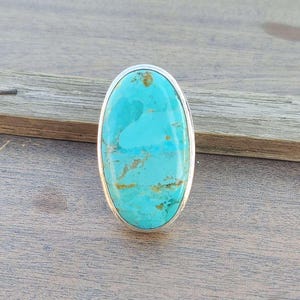 May include: Oval turquoise ring with a silver setting. The turquoise is a light blue color with brown veins.