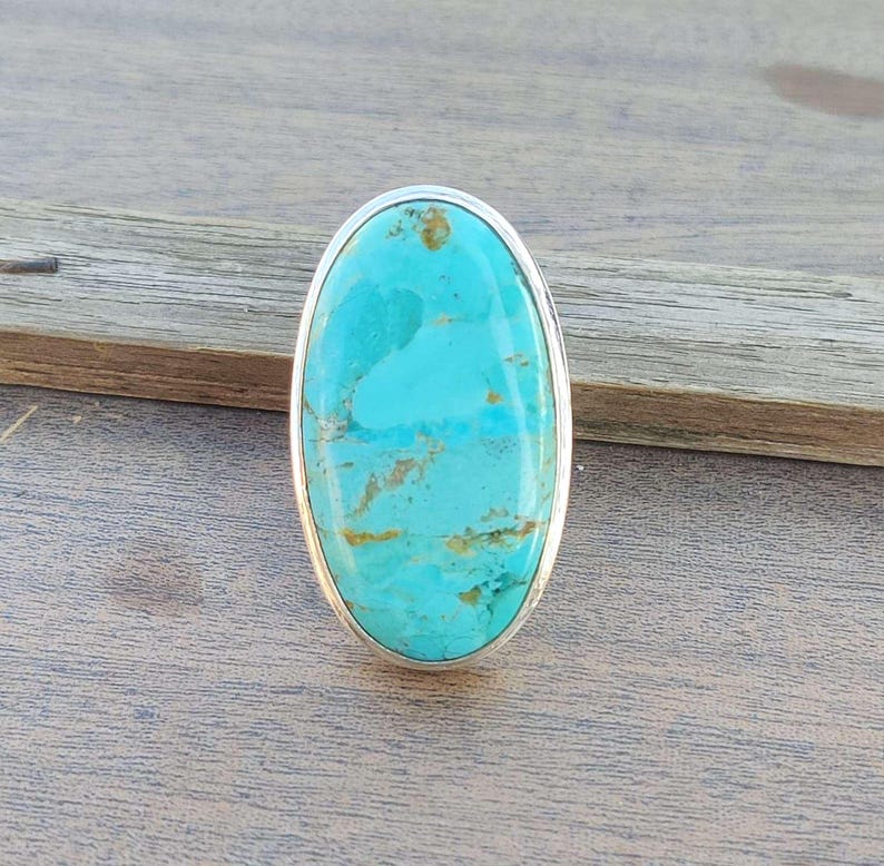 May include: Oval turquoise ring with a silver setting. The turquoise is a light blue color with brown veins.