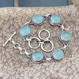 May include: A silver bracelet with a toggle clasp and six round, light blue gemstones. The bracelet has a delicate, ornate design.