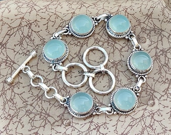 May include: A silver bracelet with a toggle clasp and six round, light blue gemstones. The bracelet has a delicate, ornate design.
