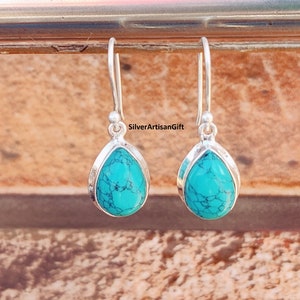May include: A pair of silver dangle earrings with turquoise teardrop-shaped stones. The earrings have a simple design and are perfect for everyday wear.
