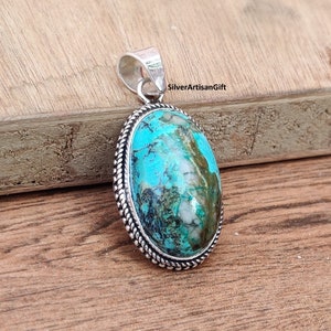 May include: A silver pendant with a turquoise stone set in a silver bezel. The stone has a blue and green color with white and brown markings. The pendant has a rope-like border around the stone.