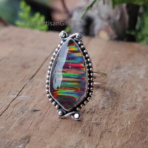 Puede incluir: Un anillo de plata con una &oacute;palo grande en forma de l&aacute;grima. El &oacute;palo muestra una vibrante gama de colores, incluyendo rojo, verde y azul, con un patr&oacute;n de rayas. El anillo tiene un borde detallado con cuentas y detalles decorativos.
