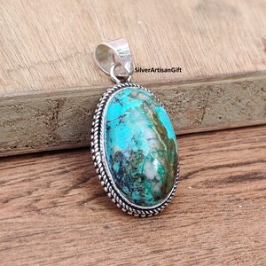 May include: A silver pendant with a turquoise stone set in a silver bezel. The stone has a blue and green color with white and brown markings. The pendant has a rope-like border around the stone.