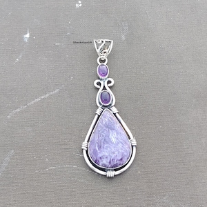 May include: A silver pendant with a large, teardrop-shaped, lavender-colored stone. Two smaller purple stones are set above the main stone. The pendant has a decorative bail and wire detailing. The text "SilverArtisanGift" is visible.
