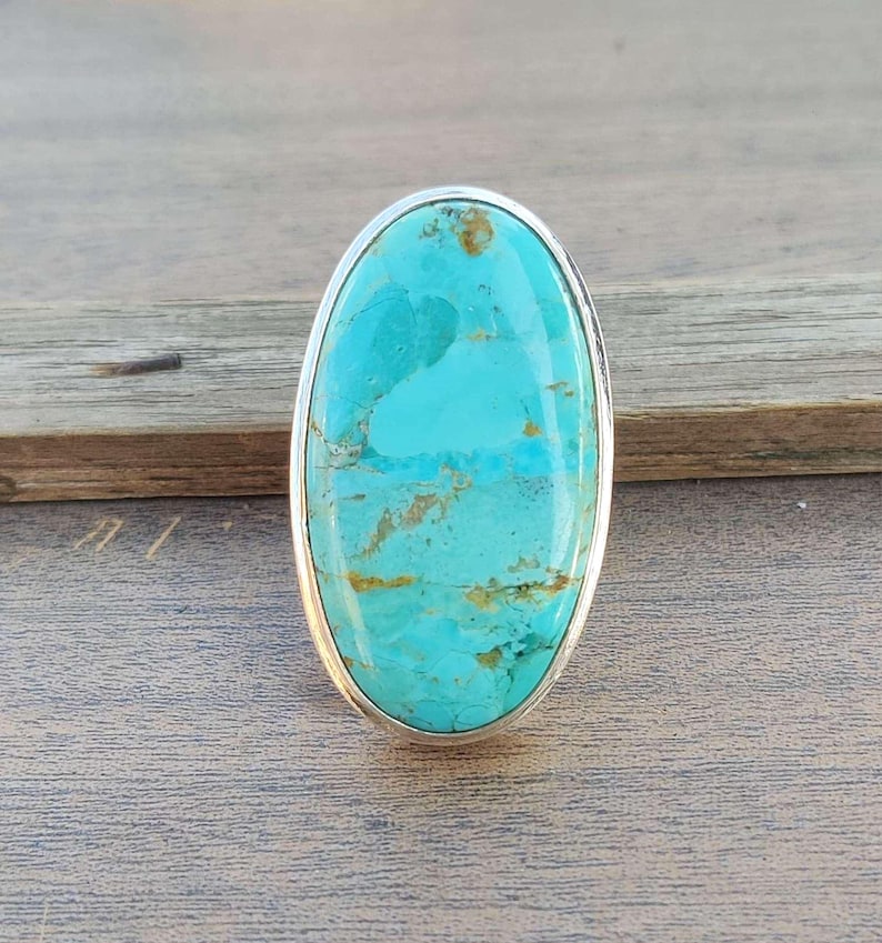 May include: A turquoise oval ring set in sterling silver. The turquoise has a blue-green color with brown veins and swirls.