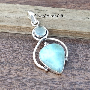 May include: A silver pendant featuring a light blue gemstone and a smaller clear gemstone. The pendant is teardrop shaped and has a silver bail.