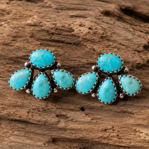 May include: A pair of silver earrings featuring clusters of bright blue turquoise stones. Each earring consists of one oval-shaped stone positioned above three teardrop-shaped stones, all set in polished silver bezels with small silver bead accents.
