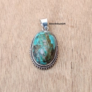 May include: A silver pendant with a turquoise stone set in an oval bezel. The stone has a green and brown marbled pattern. The pendant has a rope-like border.