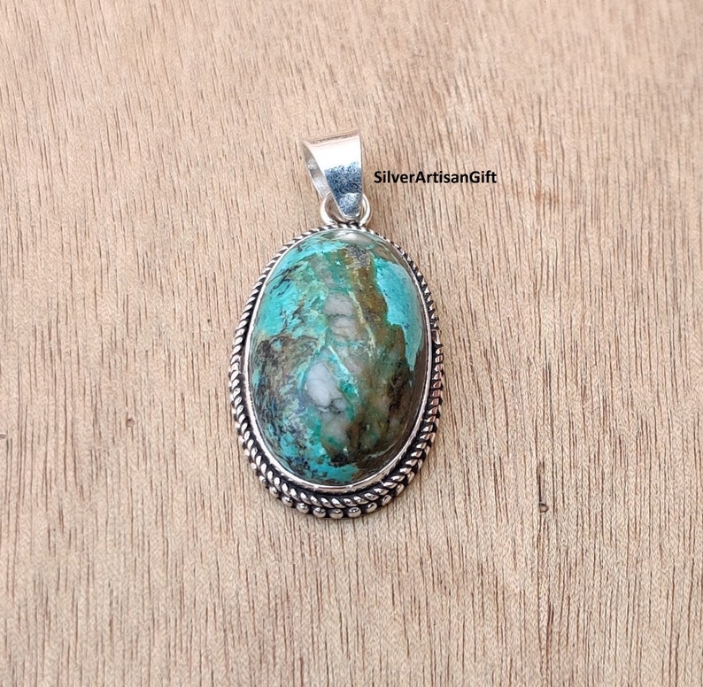 May include: A silver pendant with a turquoise stone set in an oval bezel. The stone has a green and brown marbled pattern. The pendant has a rope-like border.