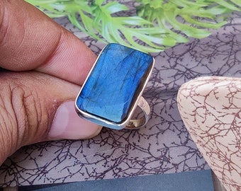Può includere: Un anello d'argento con una pietra rettangolare di labradorite blu. La pietra ha un bagliore iridescente.