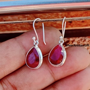 May include: A pair of silver dangle earrings with teardrop-shaped red gemstones. The earrings have a simple design and are perfect for everyday wear.