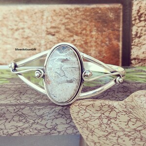 May include: A silver bracelet with a white agate stone set in the center. The bracelet has a delicate, curved design.