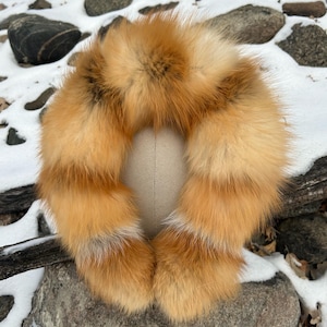 May include: A large, fluffy fox fur collar in shades of orange and white. The fur is arranged in a circle, with the ends of the fur meeting in the center. The collar is displayed on a white mannequin head.