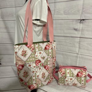 May include: A floral patchwork tote bag and matching small pouch. The tote bag has pink straps and a green interior lining. The patchwork design features roses in shades of pink and red, with green and cream accents. The pouch has a pink zipper and handle.