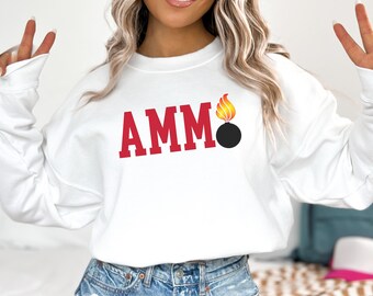 May include: White crew neck sweatshirt featuring the word "AMM" in red block letters and a graphic of a black bomb with a yellow and orange flame. The sweatshirt has long sleeves.