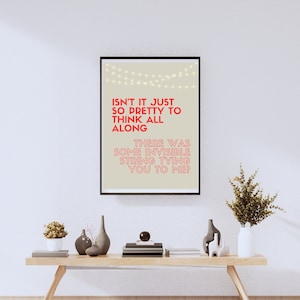 May include: A framed art print with the text "ISN'T IT JUST SO PRETTY TO THINK ALL ALONG THERE WAS SOME INVISIBLE STRING TYING YOU TO ME?" in red on a beige background. The print is displayed above a wooden coffee table with decorative items.