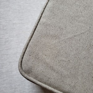 Può includere: Primo piano di un tessuto di lino beige con una texture sottile. Il tessuto ha un aspetto leggermente ruvido e tessuto.