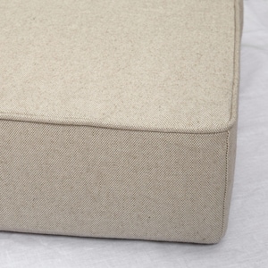Peut inclure: Un coussin rectangulaire en tissu beige avec une surface légèrement texturée. Le coussin a un design simple et épuré.