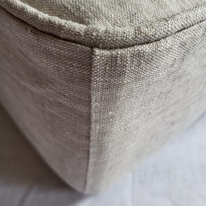 Peut inclure: Gros plan sur un coin de tissu en lin beige avec une couture qui descend le long du côté. Le tissu est texturé et a un léger brillant.