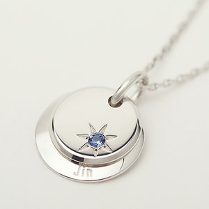 May include: Silver necklace with a round pendant featuring a blue gemstone star and the name "Jin" engraved on the bottom.