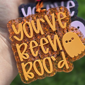 May include: Orange glitter keychain with a ghost and the text "You've Been Boo'd" in gold lettering.