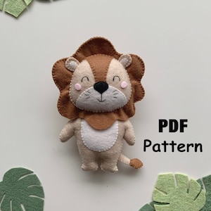 Può includere: Un modello di leone in feltro in formato PDF. Il leone è marrone e beige con un viso carino e una coda. Il modello è circondato da foglie di feltro verde.