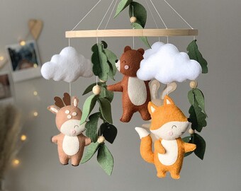 May include: A wooden baby mobile with felt woodland animals, including a deer, fox, bear, and clouds. The mobile features green felt leaves and wooden beads.