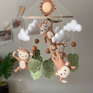 May include: A felt baby mobile with a wooden ring, four brown monkeys, three white clouds, four brown balls, and five green leaves. The mobile also features a yellow sun with orange rays.