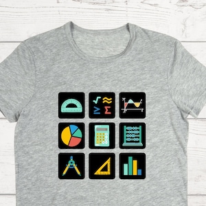 May include: A gray t-shirt with a graphic of nine black squares, each containing a different math symbol or tool. The symbols include a protractor, a square root symbol, a summation symbol, a graph, a pie chart, a calculator, an abacus, a compass, a ruler, and a bar graph.