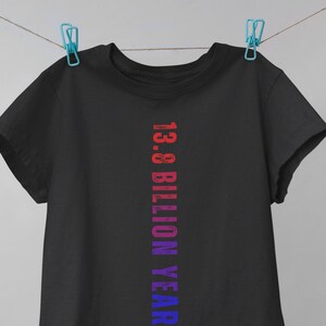 May include: Black t-shirt with a vertical graphic design in shades of red, pink, purple, and blue. The graphic reads "13.8 Billion Years".