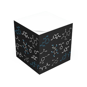 May include: A black notepad with a white top and a white sticky note. The notepad is covered in white and blue chemical formulas on a black background.