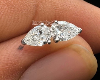 Könnte beinhalten: Ein Paar tropfenförmige Diamantohrringe. Die Diamanten sind in einer Fassung aus Silber oder Weißgold gefasst. Die Ohrringe werden in der Hand einer Person vor dunklem Hintergrund gehalten. Der Text "Naturesparkjewel" ist sichtbar.