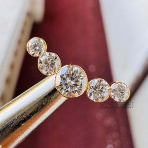 Può includere: Un orecchino a cerchio in oro con cinque pietre rotonde di zircone cubico trasparenti disposte in una linea curva.