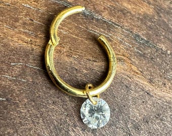 May include: A gold hoop earring with a small, clear, round gemstone dangling from it.
