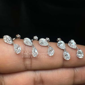 May include: A collection of silver earrings with a pear-shaped design. Each earring features a larger pear-shaped stone at the bottom and a smaller one at the top. The earrings are displayed against a dark background.