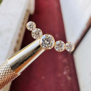 May include: A gold ear cuff with five clear round cubic zirconia stones set in a curved line.